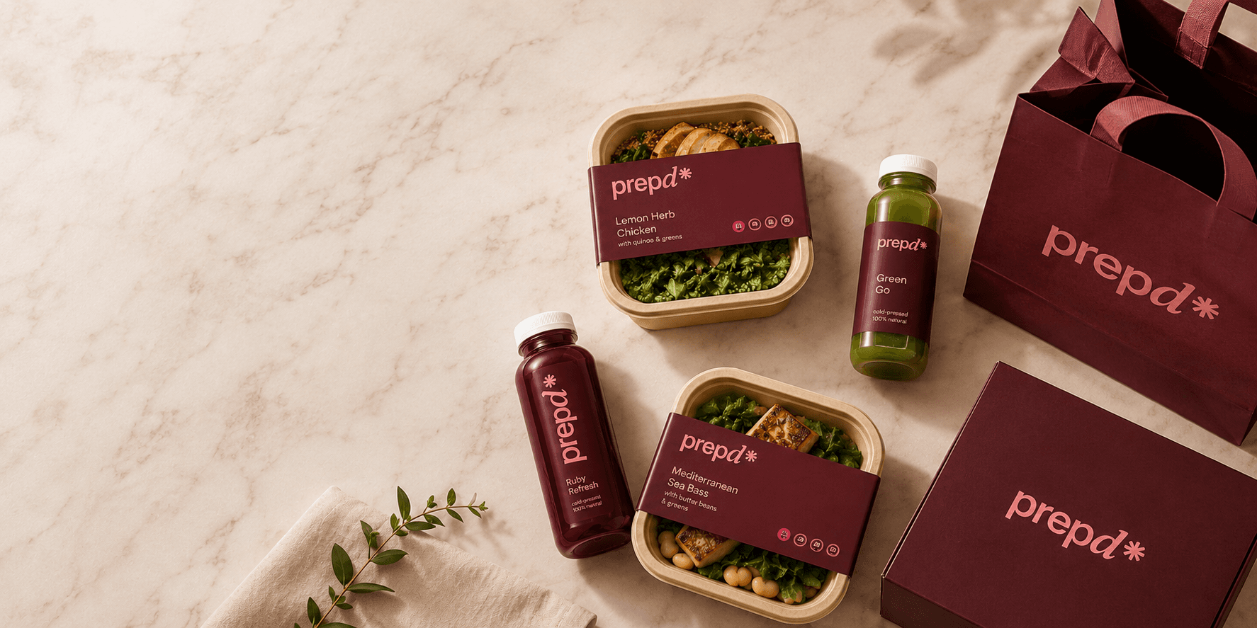 Prepd meal trays, cold-pressed juices and branded packaging arranged on marble